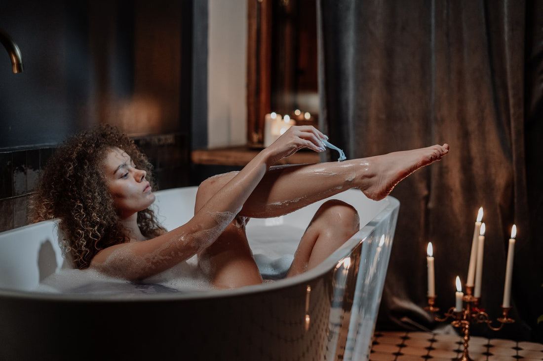 en kvinna rakar sina ben i badkaret