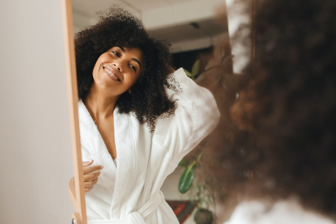 en glad kvinna framför spegeln med friskt hår tack vare bättre hårvård