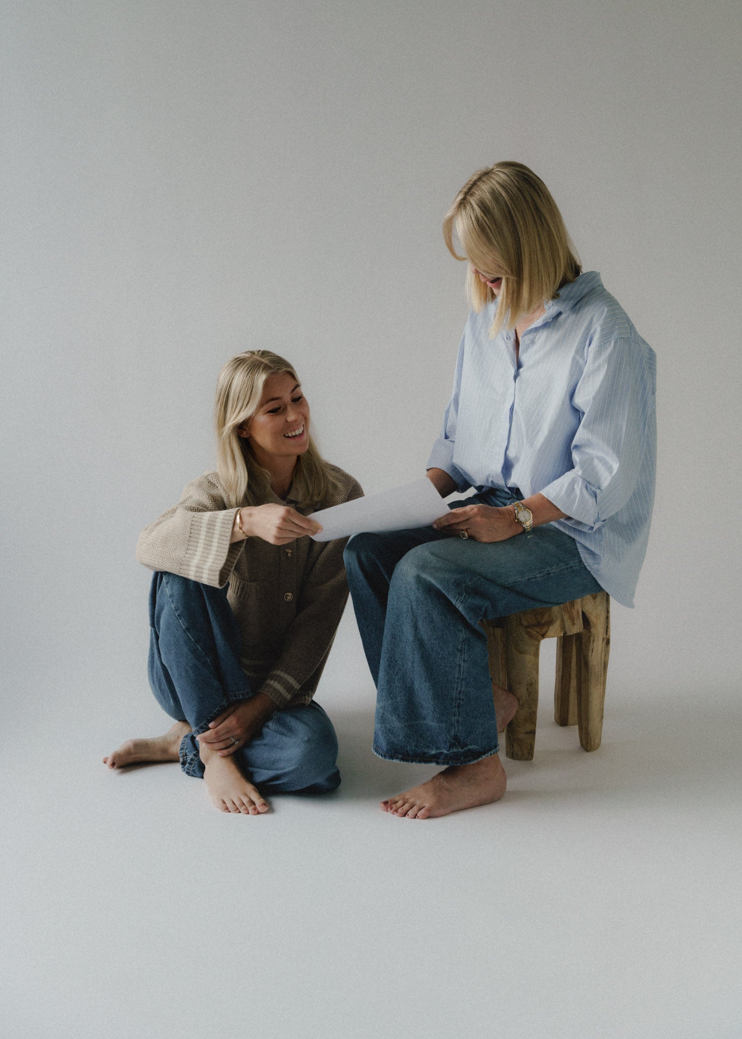 Lovisa och Christina, grundare, sitter och läser ett papper mot ljusgrå bakgrund